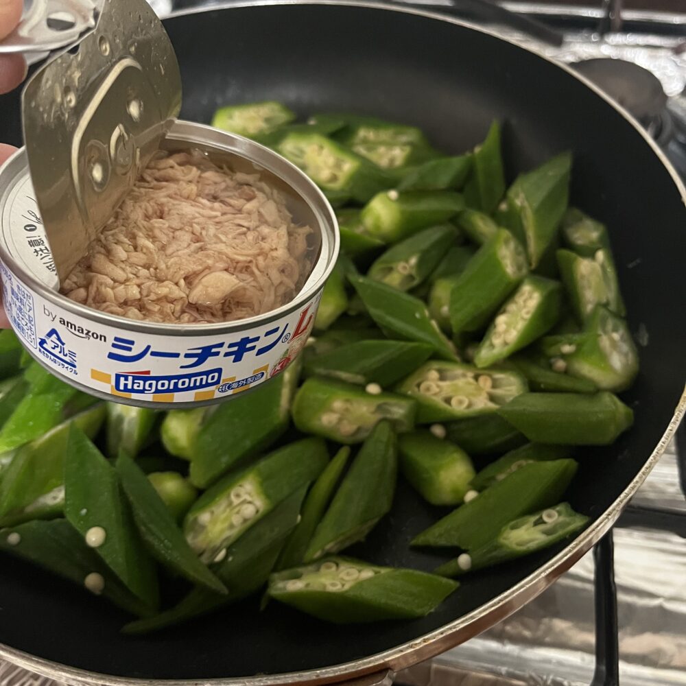 フライパンのオクラにシーチキンの缶を入れるところ