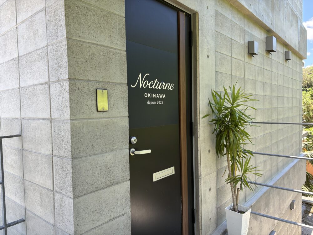 Nocturne Okinawaの入口。黒いドアに白い文字でNocturne OKINAWA depuis 2025