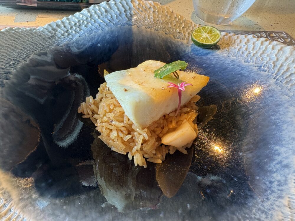 Nocturne Okinawaの魚料理。サンゴのような大きな器にリゾットと白身魚、シークヮーサーが添えられている