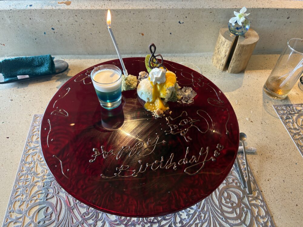 Nocturne Okinawaのバースデーデザートプレート。赤いガラスの大皿にHappy Birthdayの文字とキャンドル、ト音記号の飾り